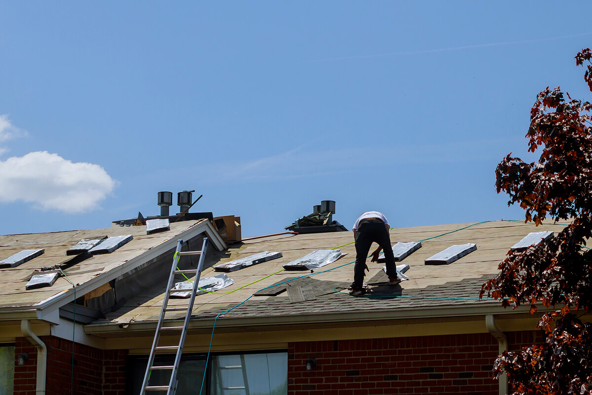 Worker installing shingles on a residential roof under blue sky.
